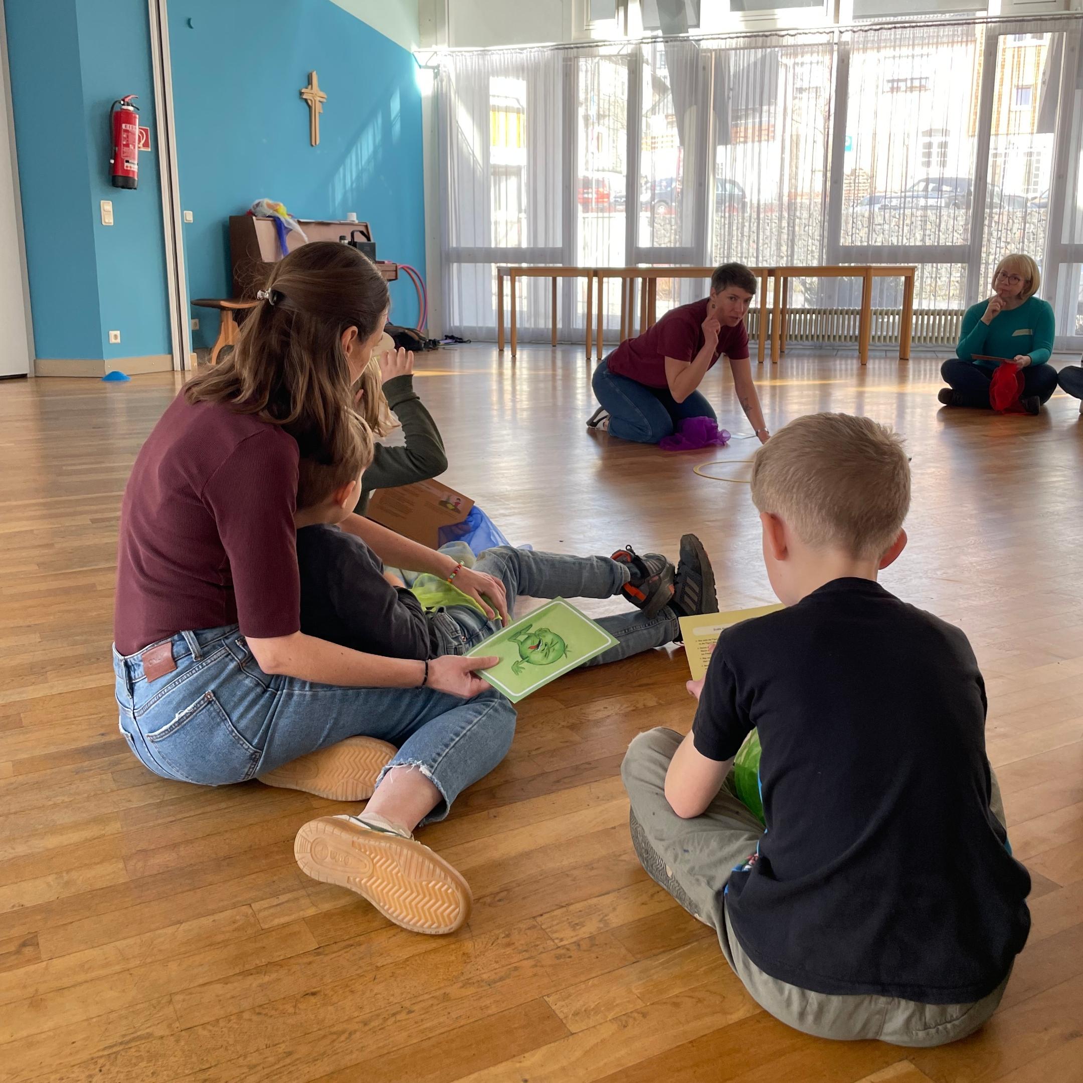Eltern und Kinder sitzen im Sitzkreis und haben jeweils ein Blatt in der Hand