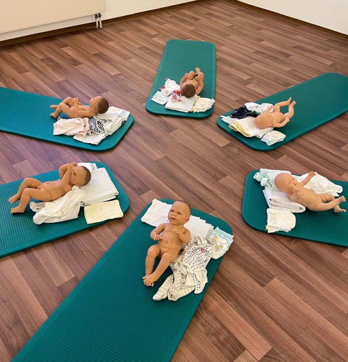 Auf einem Holzboden liegen 6 grüne Gymnastikmatten mit jeweils einer Babypumpe und Zubehör zum Wickeln